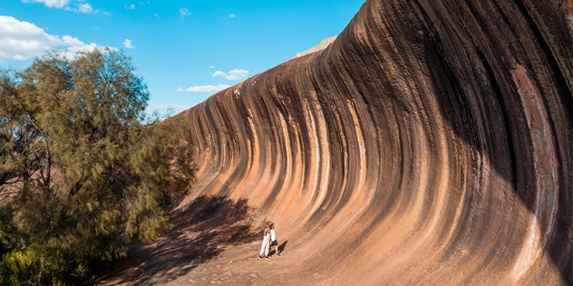  Two people standing next to fourteen metre tall rock wall with a deep curve and colour gradation that looks like an ocean wave.