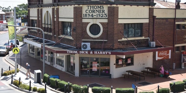 heritage red brick two storey building that spans a street corner with Thom's Corner 1894-1923 painted on the facade and Thom, Dick and Harry's painted on the awning