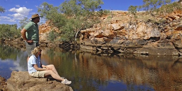 two people resting on a rock looking across the creek