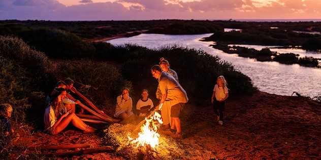 A small gathering of kids and adults around a riverside bonfire at sunset at Gutharraguda, Western Australia. 