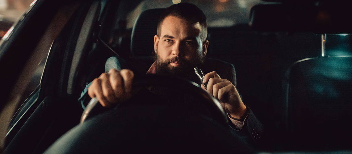 Man vaping behind the steering wheel of a car