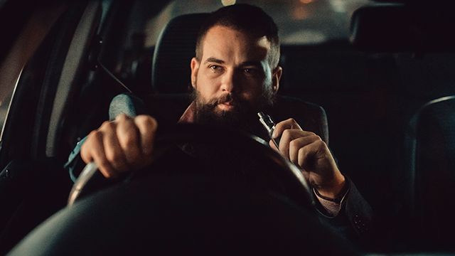 Man vaping behind the steering wheel of a car